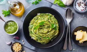 Spaghetti z pesto i bazylią w czarnej misce, obok sos, orzeszki piniowe, czosnek i parmezan.