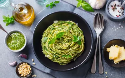 Spaghetti z pesto i bazylią w czarnej misce, obok sos, orzeszki piniowe, czosnek i parmezan.